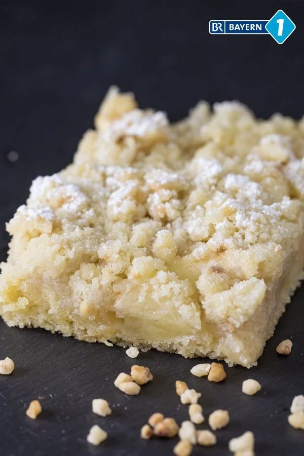 Apfelstreuselkuchen vom Blech auf einem Tisch serviert, mit frischen Äpfeln und Streuseln.