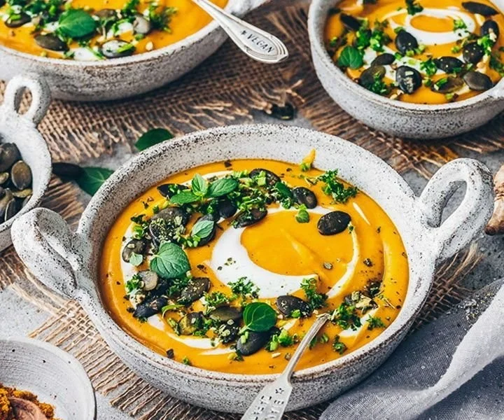 Veganer Kürbissuppe in einer Schüssel, dekoriert mit frischen Kräutern.